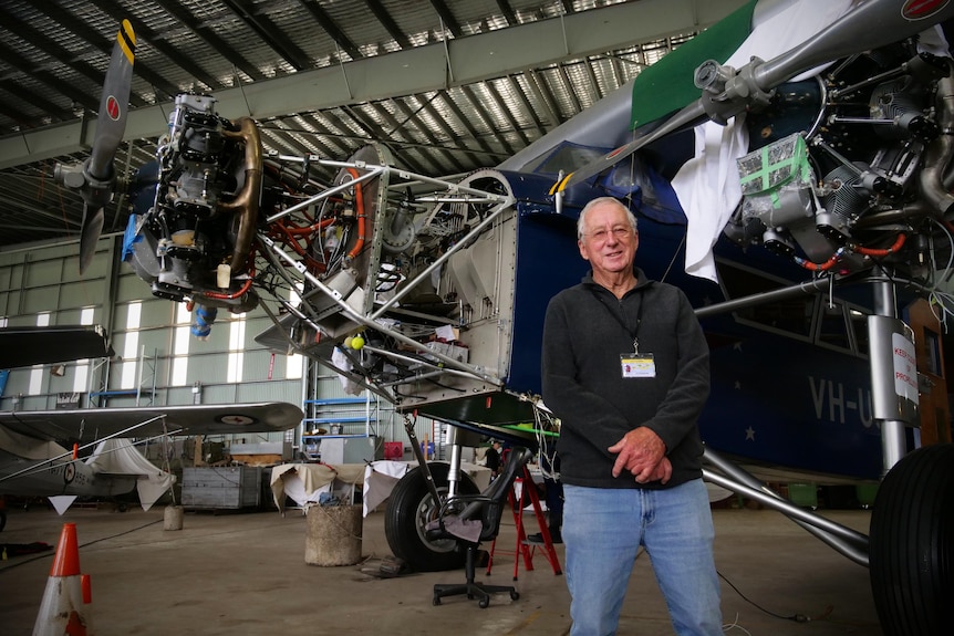 Jim stands in a dark sweater and jeans in front of the Southern Cross replica with engines and accessories on display.
