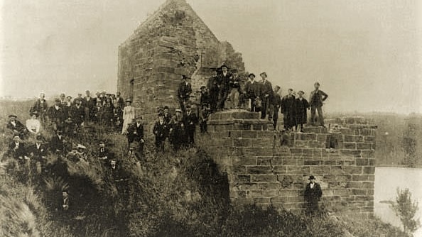 Black and white image of people posing at ruins of a brick structure.