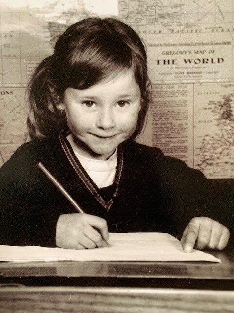 Black and white image of a 7 year-old-girl smiling in front of a map of the world. 
