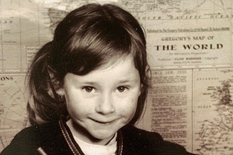 Black and white image of a 7 year-old-girl smiling in front of a map of the world. 