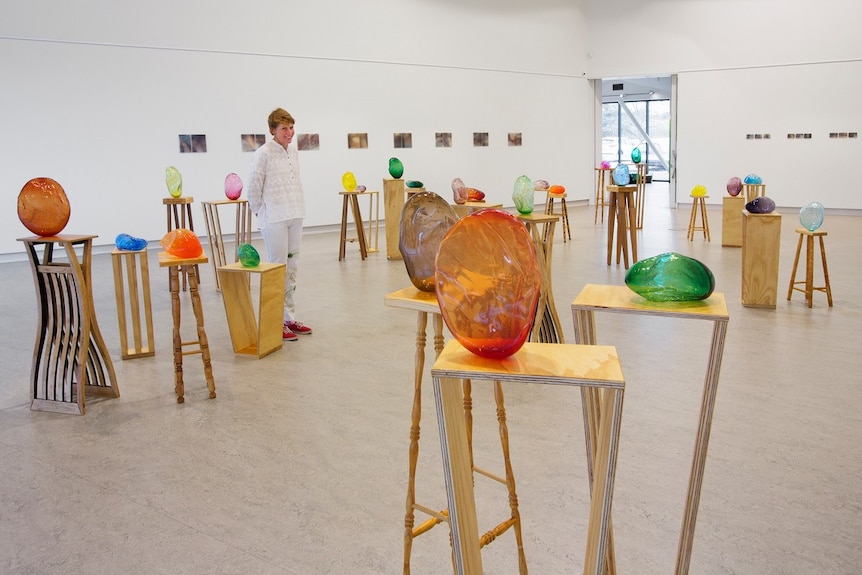 Different 'hugs' sit on plinths placed around a large exhibition space, Catherine standing among them.