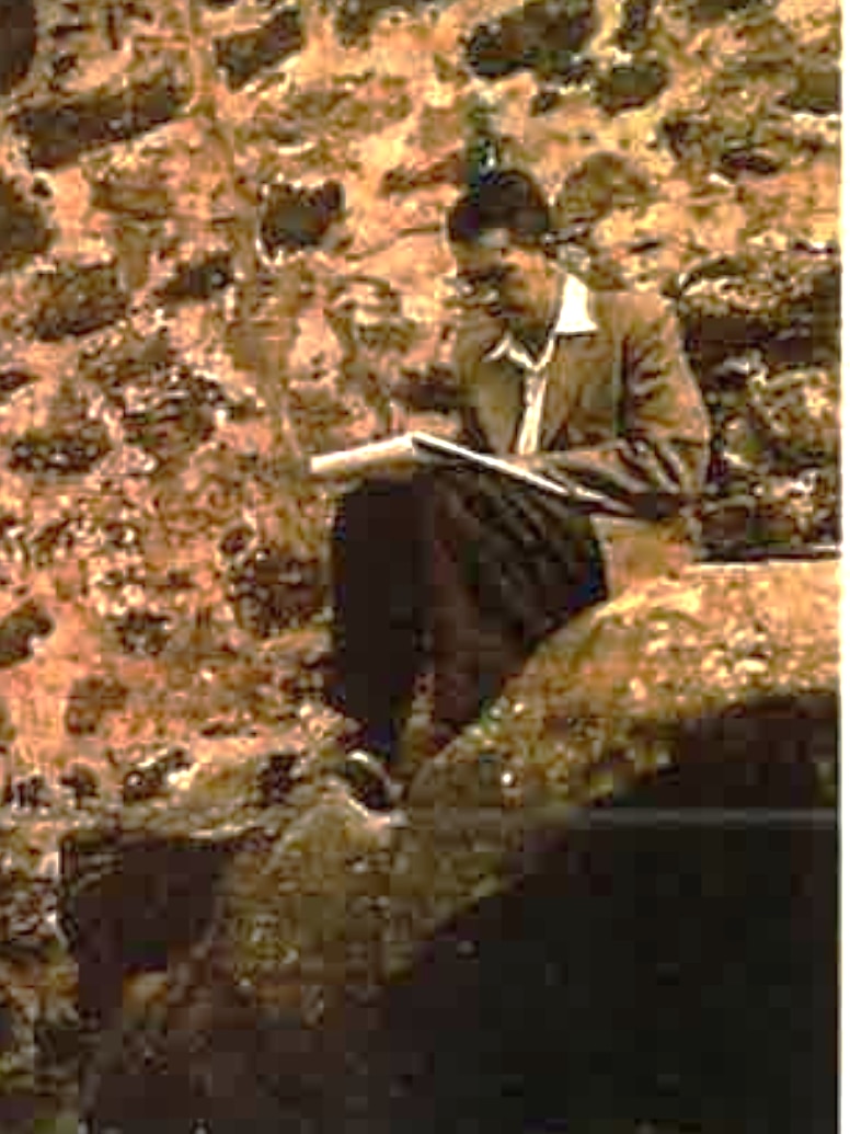 a black and white photo of a man sitting on a rock drawing