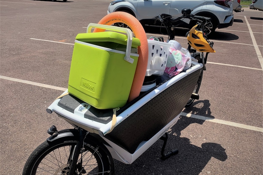 A box bike in a carpark containing a green esky and other stuff.