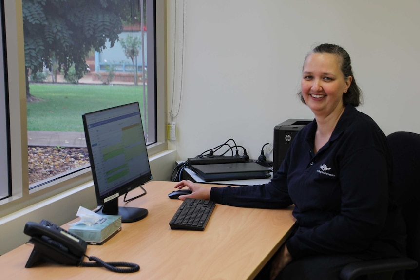 Doctor Bec Jacobs looks at the camera and smiles while using a computer in her office.