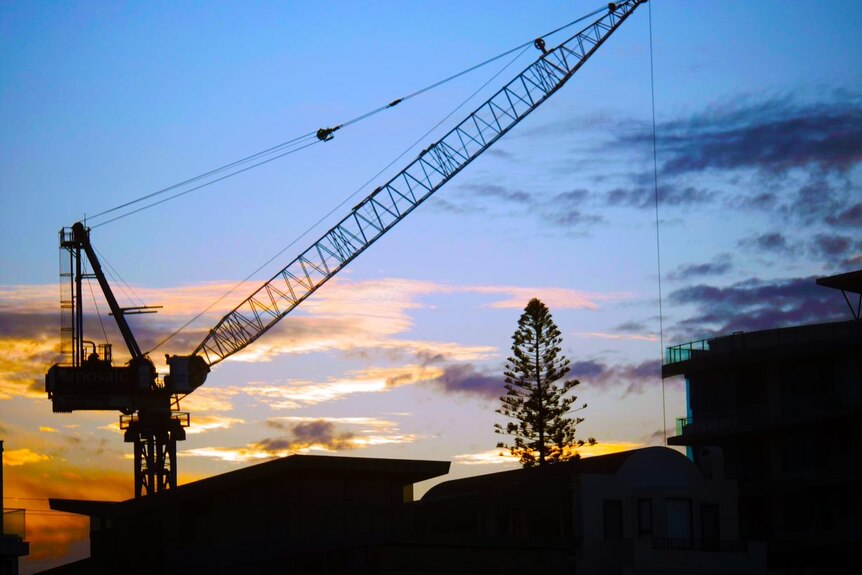 Silhouette of a crane building on high rises against sunset