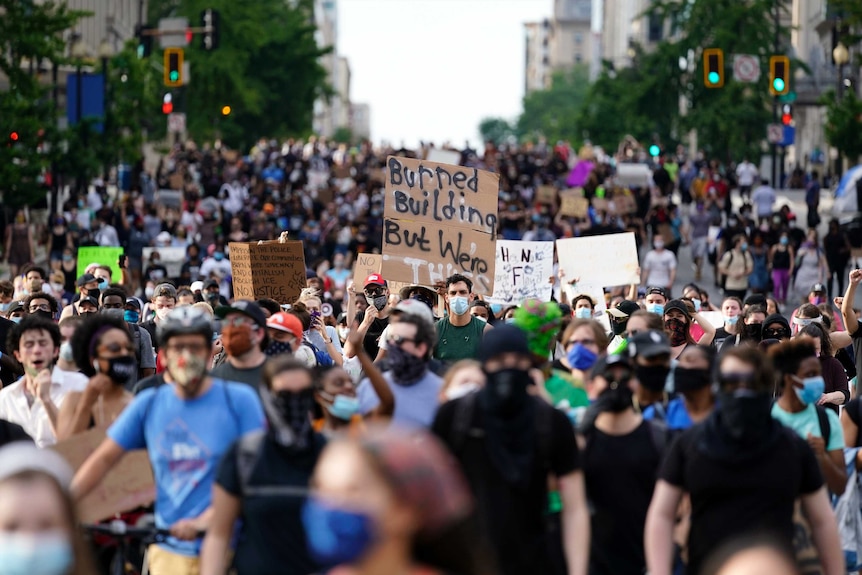 At least hundreds of people are seen walking in protest during daylight, many holding placards.