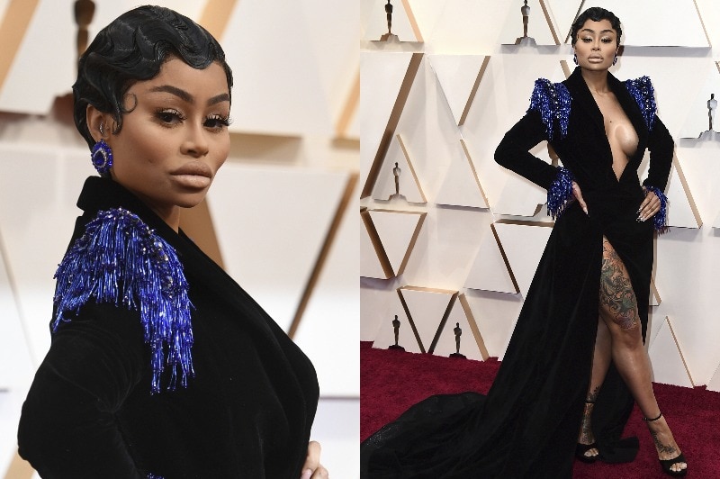 Blac Chyna wearing a long-sleeve black gown with a high slit and blue tinsel fringing on the shoulders.