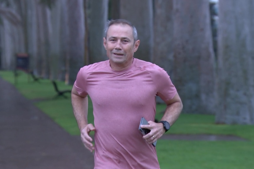 A man in a pink shirt jogging while carrying a phone.