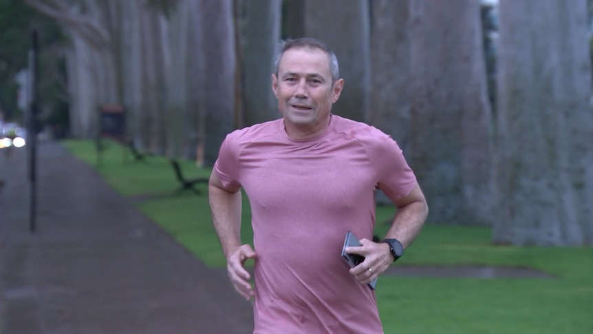 A man in a pink shirt jogging while carrying a phone.