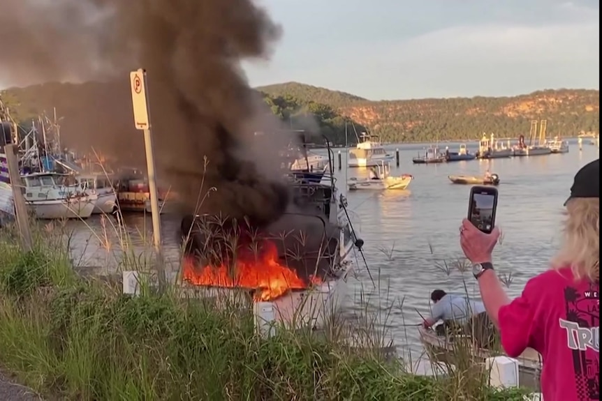 people filming a burning boat