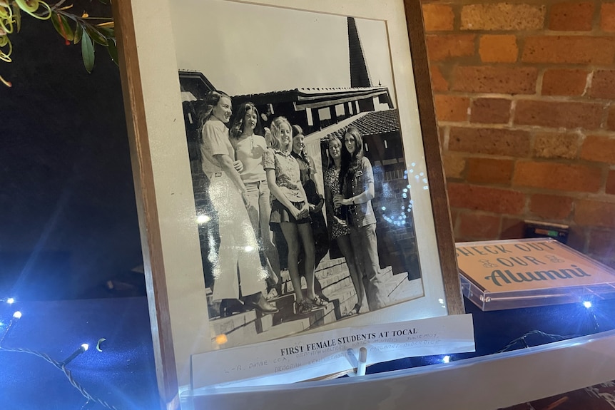 A picture frame sits on a table, with a black and white image of seven young women from the 1970s at Tocal College