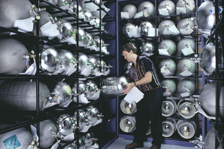 Man handling large metallic bottles inside a room.