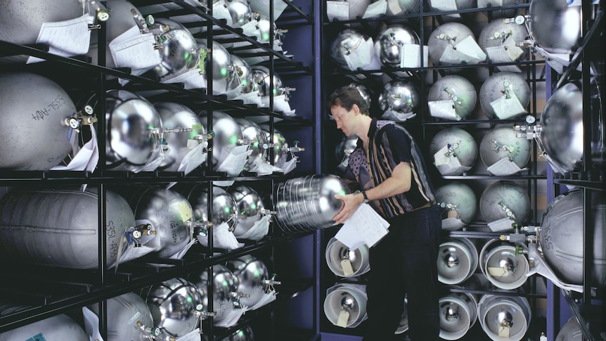 Man handling large metallic bottles inside a room.