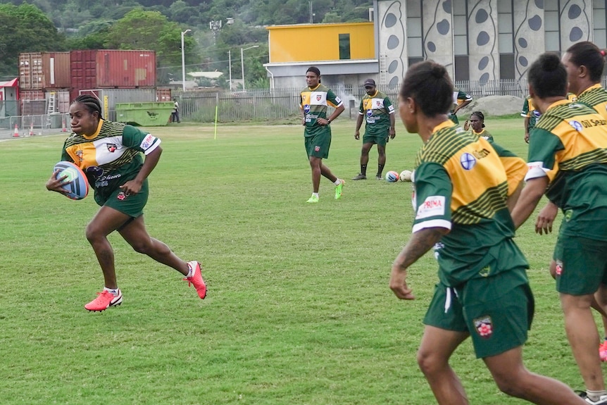 A women runs with a rugby league ball while others watch on