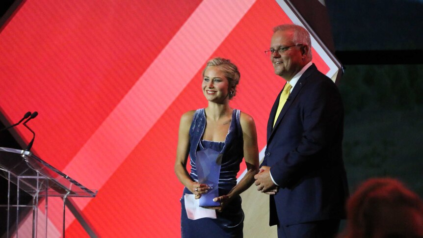 Grace Tame smiles with her award, standing with Prime Minister Scott Morrison.