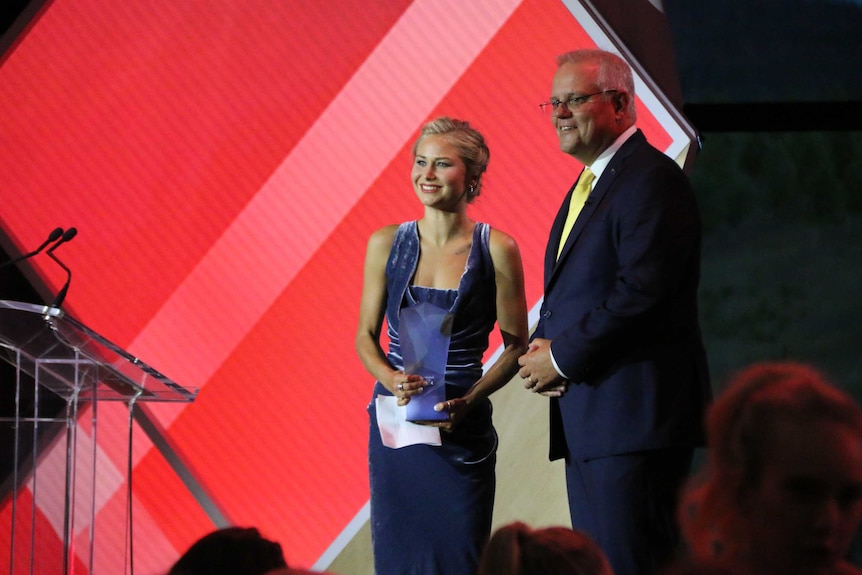 Grace Tame smiles with her award, standing with Prime Minister Scott Morrison.