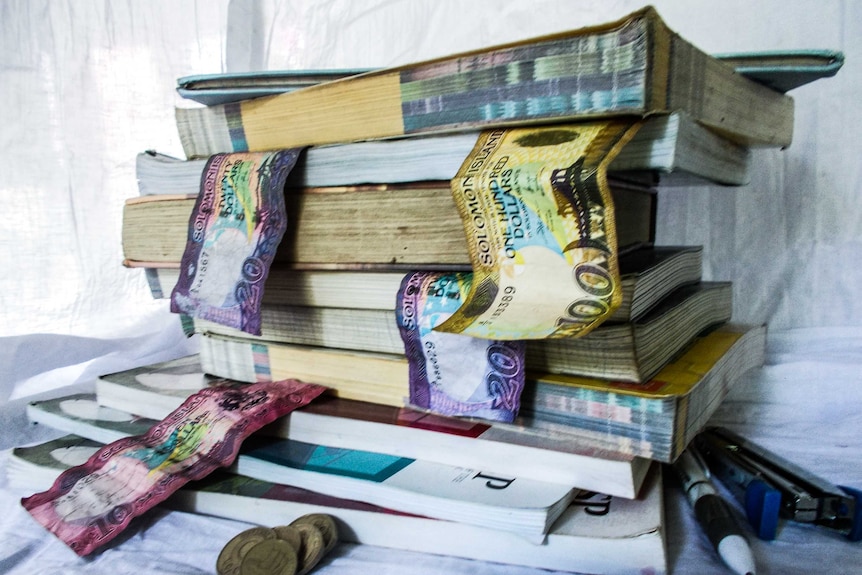 A pile of schoolbooks with money notes place in between the pages.