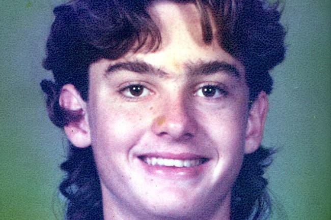 A teenager with wavy hair smiles at camera