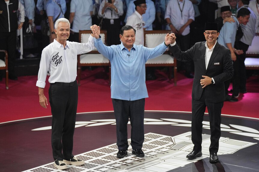 Ganjar Pranowo, Prabowo Subianto and Anies Baswedan hold hands smiling on a stage