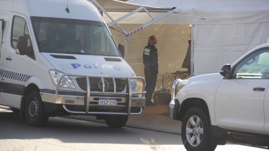 A police van sits parked on the side of a road next to a white tent with a forensics officer standing inside.