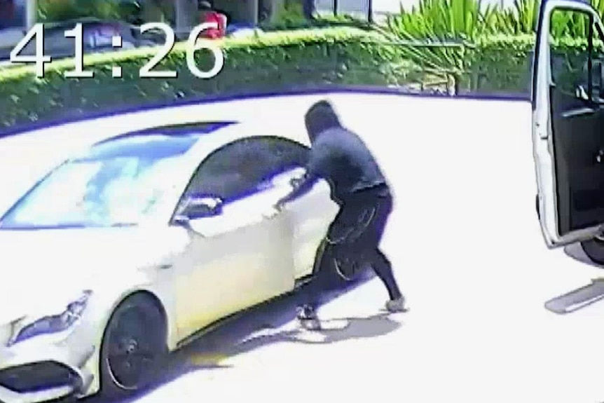 A man in a black hoodie opens the door of a white car