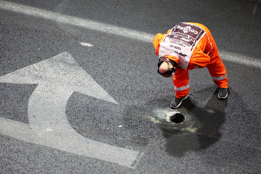 A man in a high-viz outift leans over to look at an open drain on a Formula 1 street race track in Las Vegas.