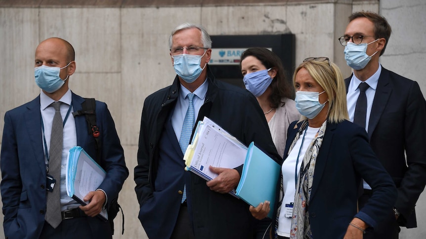 A group of people in suits and face masks stand outside on the stairs of a building.