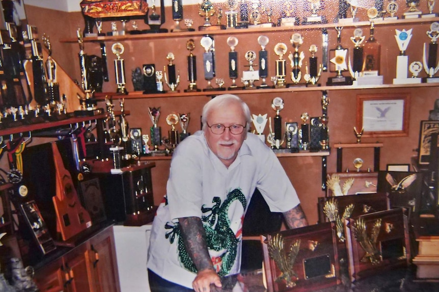 Tattoo artist Les Bowen stands in a room full of trophies