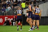 A Fremantle AFL forward puts his hands over his head in frustration as teammates look dejected during a game.