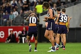 A Fremantle AFL forward puts his hands over his head in frustration as teammates look dejected during a game.