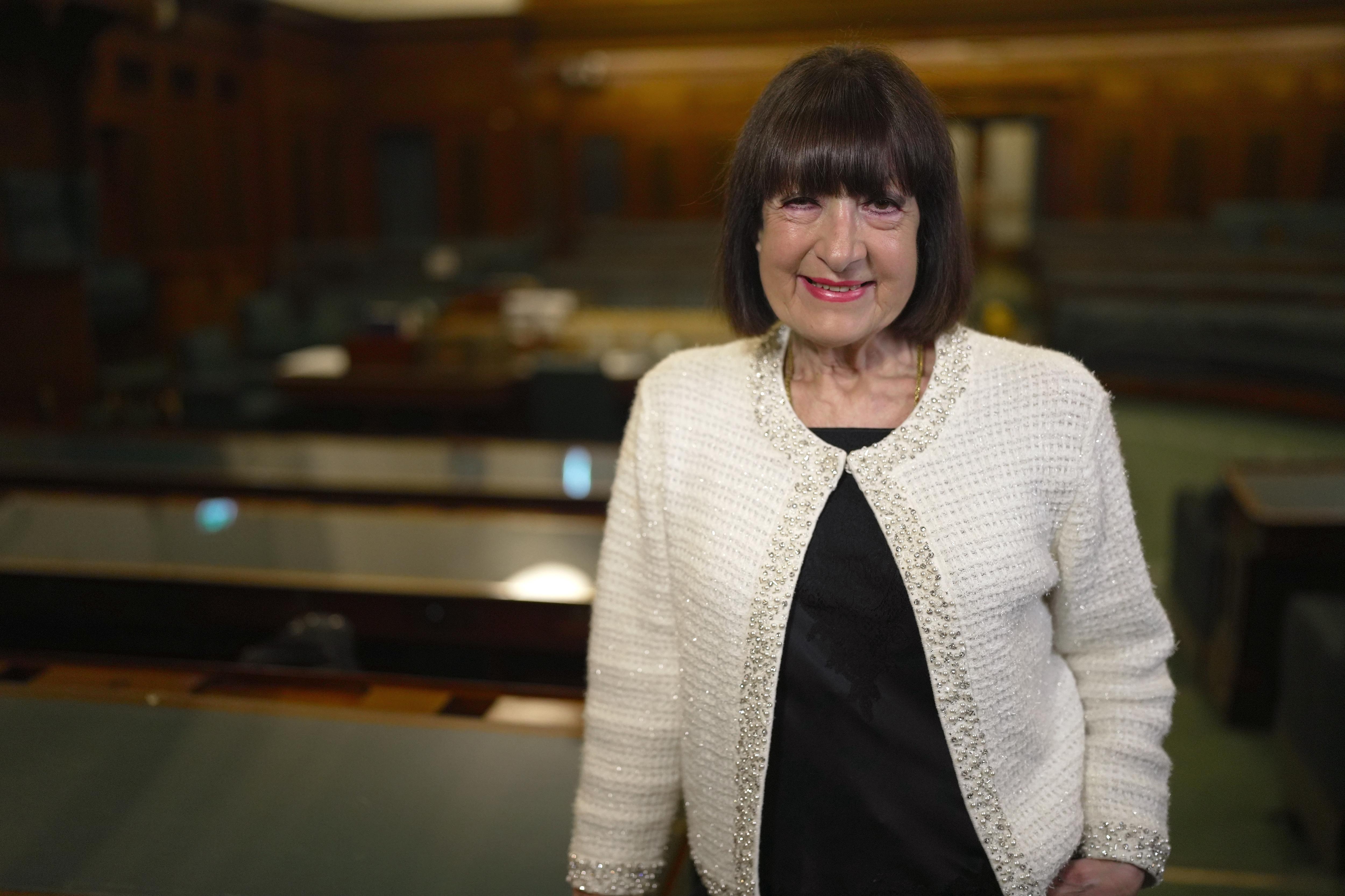 A smiling woman standing in a chamber of parliament.