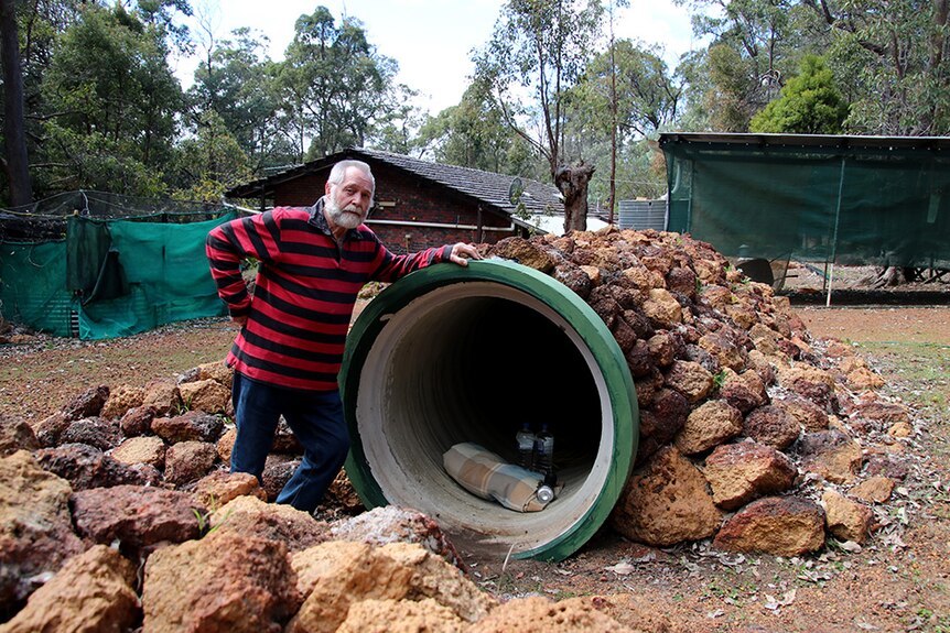 A man stands near a large concrete pipe that is covered with rocks.