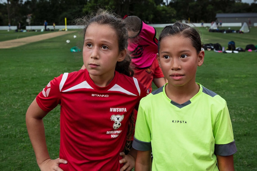Two young girls in sports clothes look on