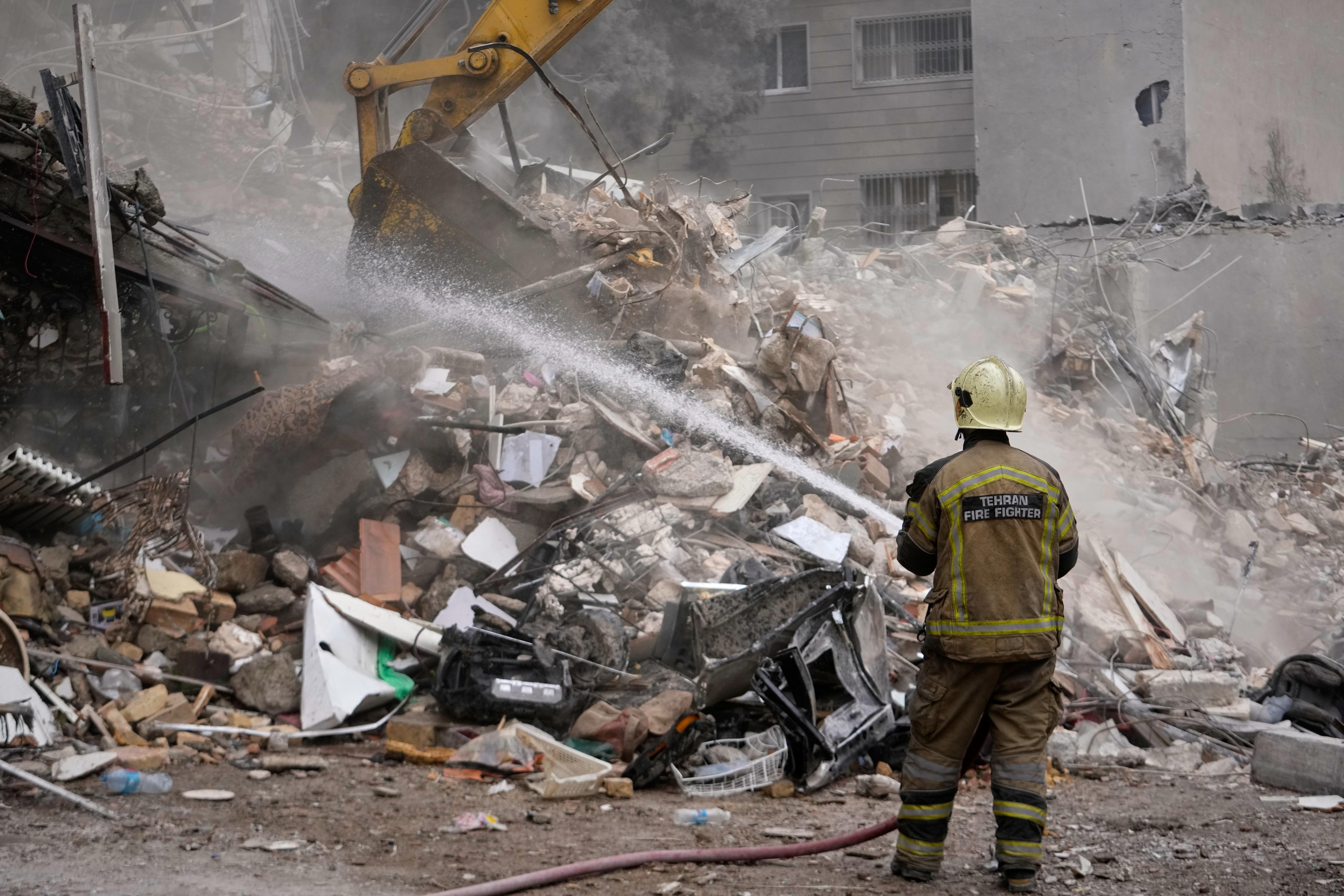 A firefighter holds a hose in front of a damaged apartment building.