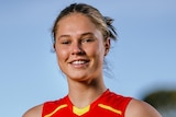 A Gold Coast Suns AFLW recruit stands with the ball held in her left hand.