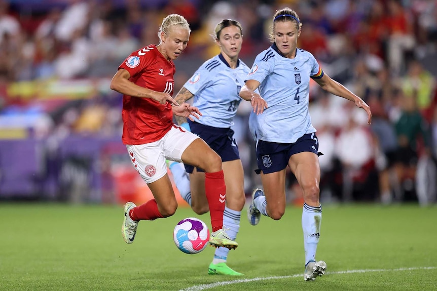 Pernille Harder of Denmark controls the ball while being pursued by two opposition players.