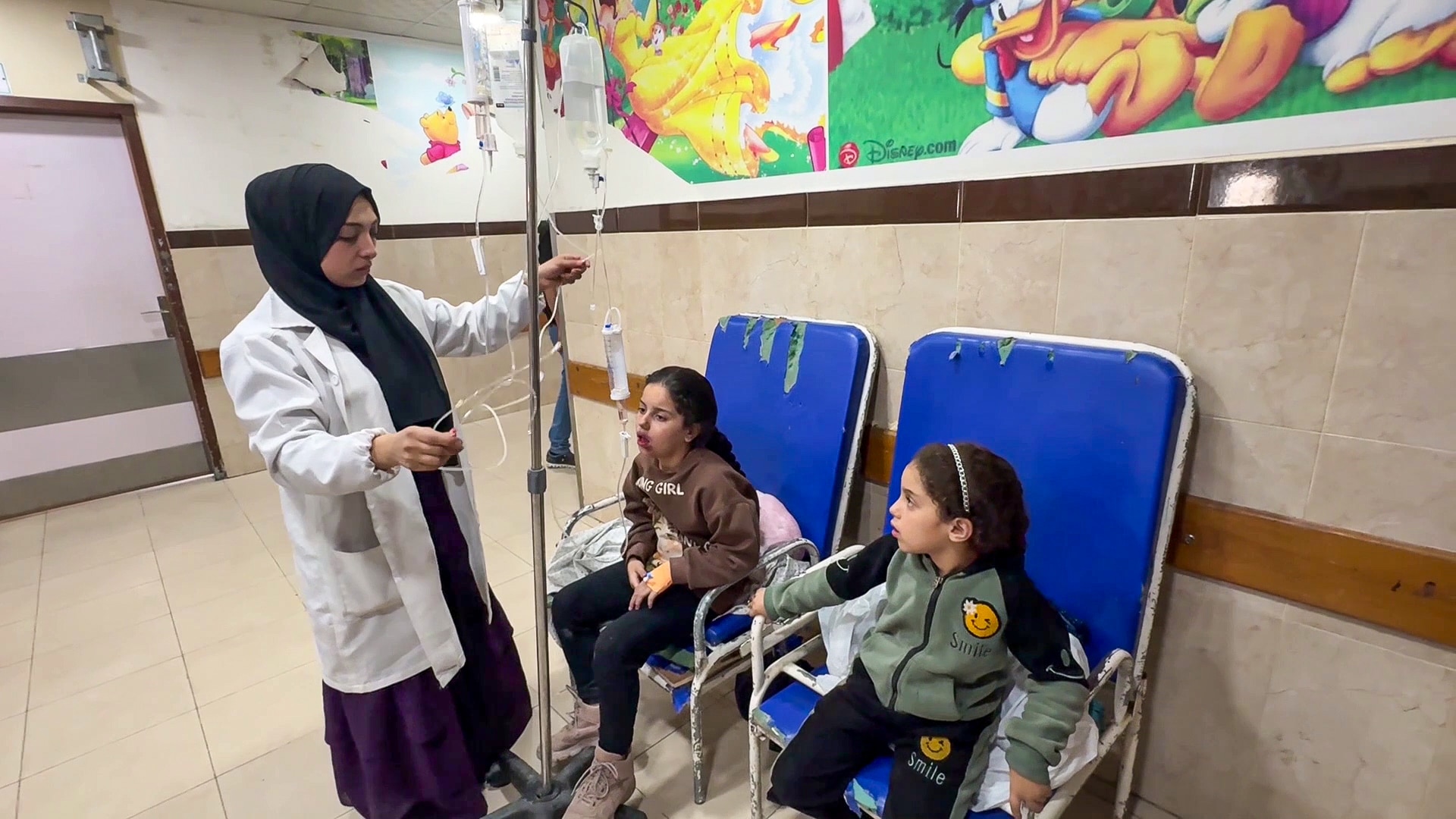 Nour Al-Tarabish arranges an IV drip to treat two girls who are sitting inside a hospital.