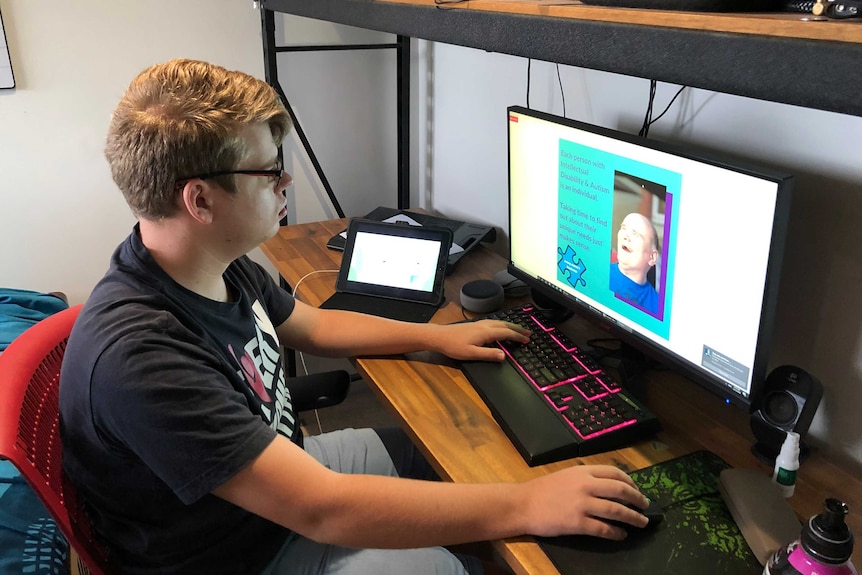 Corey Burke sits at a computer, the screen shows a slide explaining people with intellectual disabilities are individuals.