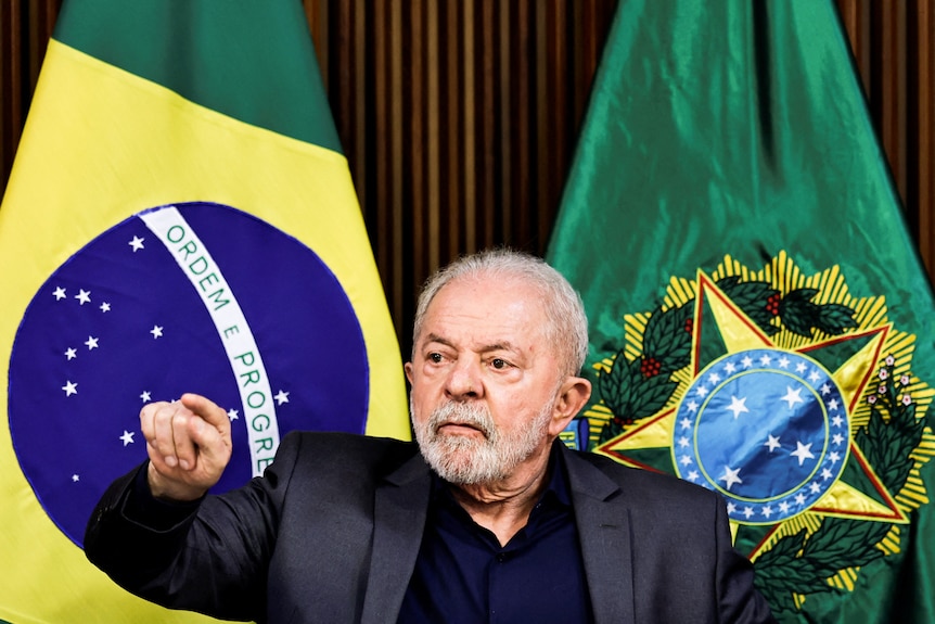 Luiz Inacio Lula da Silva wears a suit and gestures during a meeting at a podium.