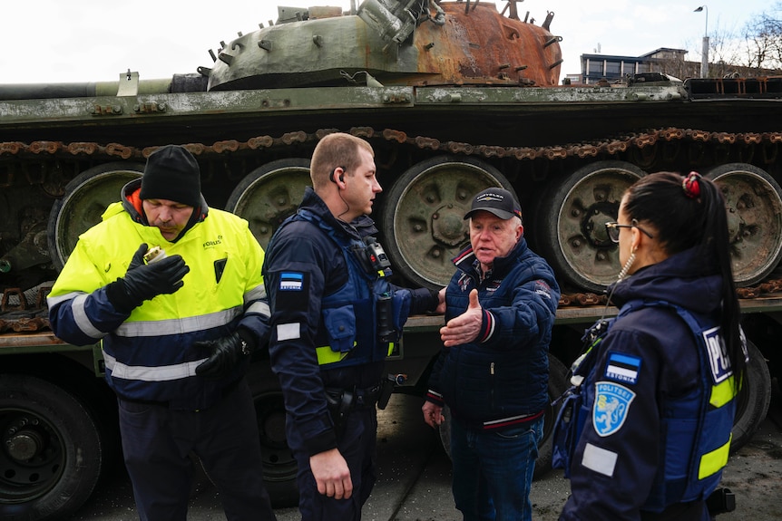 Security guards speaking with man (centre) who placed a candle next to a destroyed Russian tank on display.