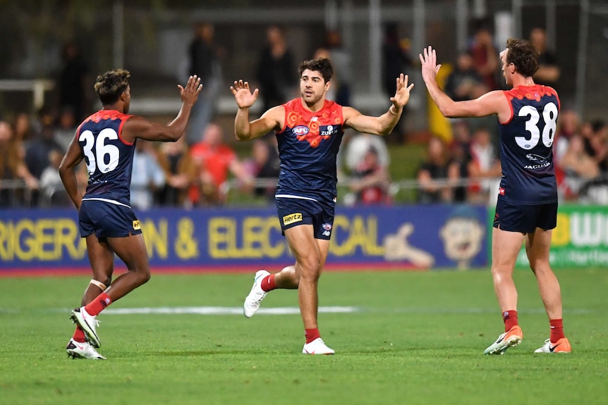 A Melbourne Demons AFL player runs as he high fives two of his teammates against St Kilda in Alice Springs.