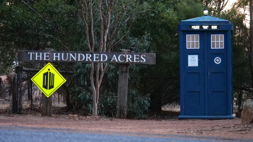 The TARDIS phone box next to a sign labelled "The Hundred Acres" and a high vis sign with the Dr Who logo.