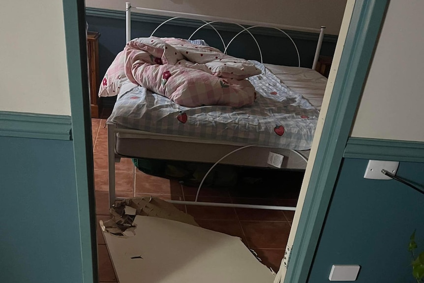 A bedroom with a broken door lying on the floor in front of an unmade bed.
