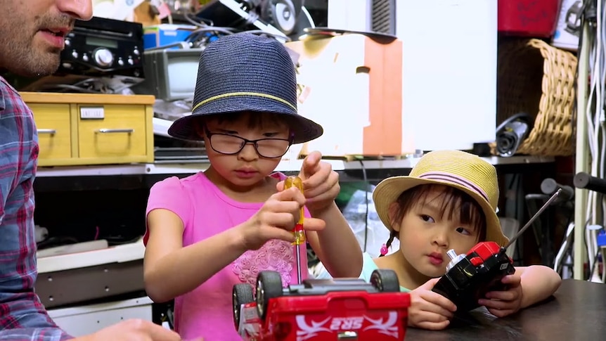 Girl using screwdriver to fix a toy car while a girl holding a remote control watches on