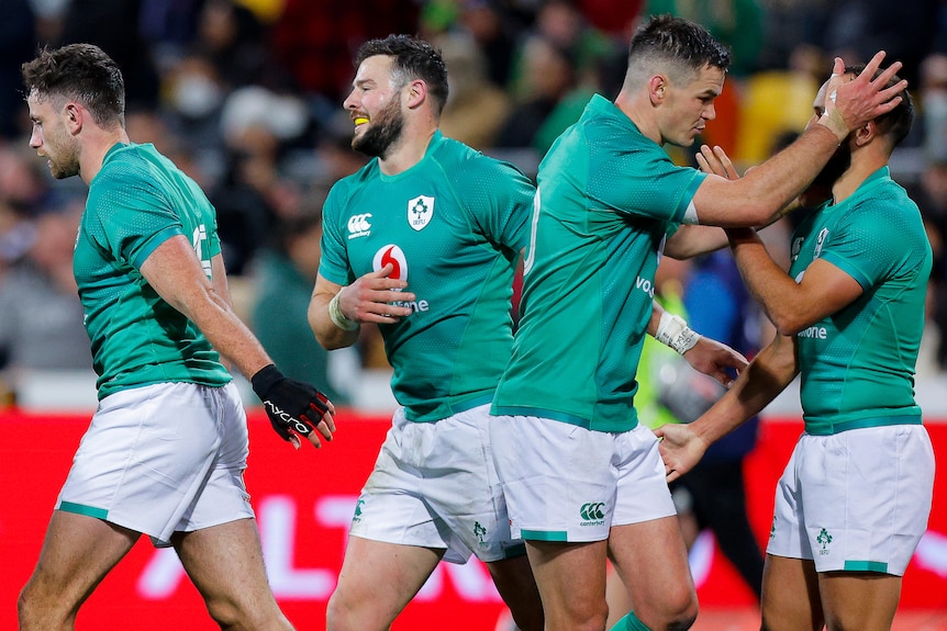 Four male Irish rugby internationals celebrate a try against the All Blacks.