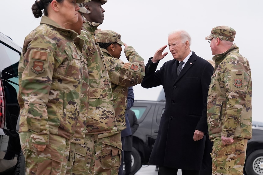 Joe Biden salutes three uniformed service members as he arrives at an air force base.