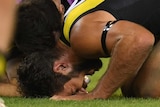 Alex Rance, curled up and on all fours, winces in pain as a doctor leans over him.