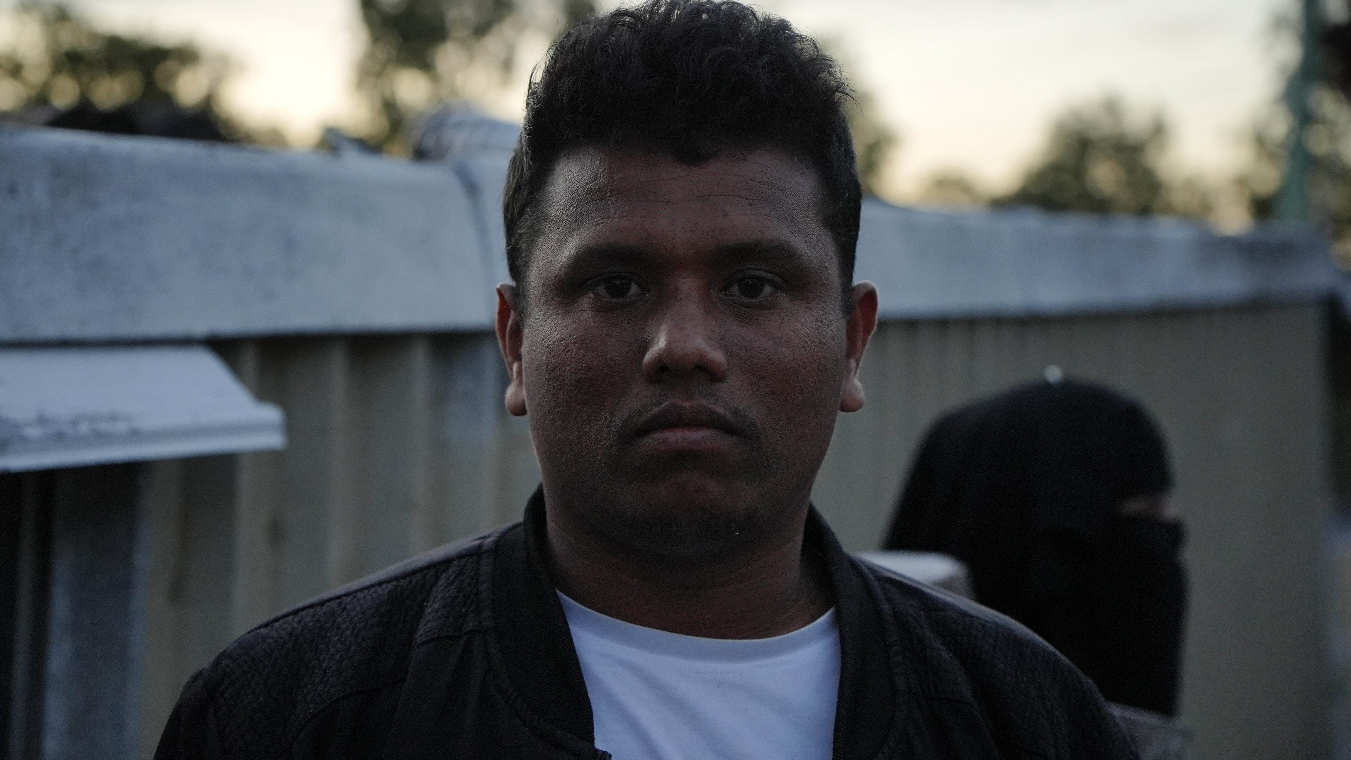 A man with a white t shirt and black jacket looking into the camera.