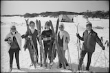 Black and white photo of group of adult skiers in warm clothes holding skis in the snow