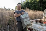 A Japanese farmer posese for photographs with a bag of human faeces-made fertiliser near some crops.